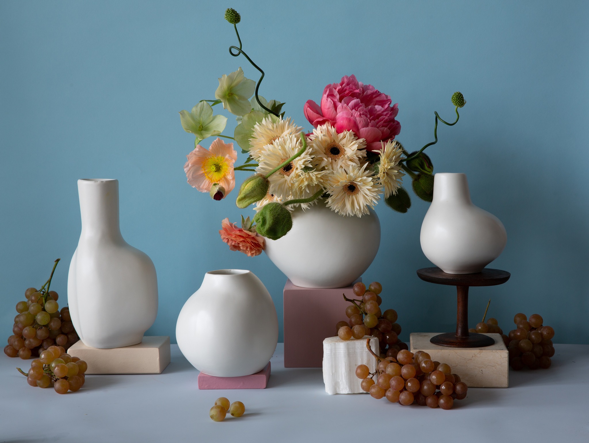 Various sizes of white porcelain vases with flowers and fruit accents.